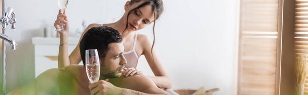 Pretty woman touching muscular man with glass of champagne in bathtub, banner  - Фото, зображення