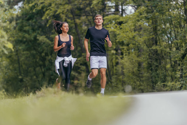 Jonge fitte paar atleten hardlopen op de weg in een bos. - Foto, afbeelding
