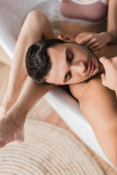 Top view of blurred woman touching bearded boyfriend in bathtub  - Foto, immagini