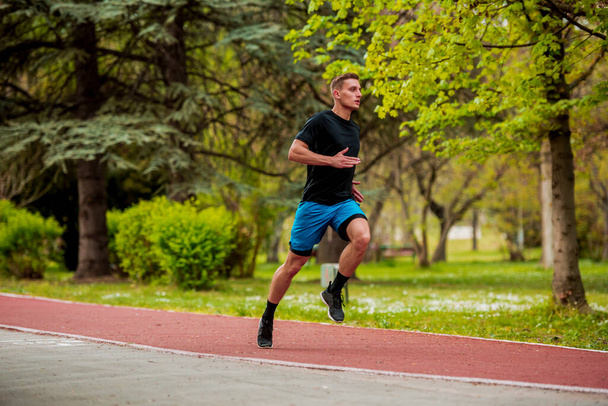Atrakcyjny biegacz biegający po torze biegowym w parku miejskim. Trening i ćwiczenia dla wytrzymałości - fitness zdrowy styl życia koncepcja outdoor - Zdjęcie, obraz