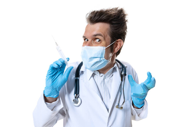 Portrait of funny doctor with stethoscope and face mask on white studio background. Looks sad, serious. Concept of healthcare and medicine, war, help, treatment - Foto, afbeelding