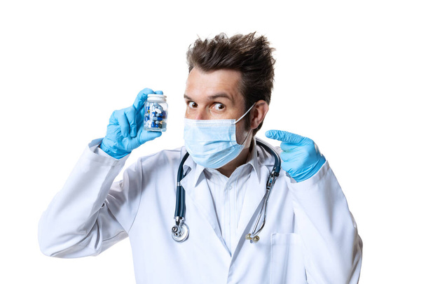 Male young doctor with stethoscope and face mask on white studio background. Looks sad, serious. Concept of healthcare and medicine, war, help, treatment - Photo, Image