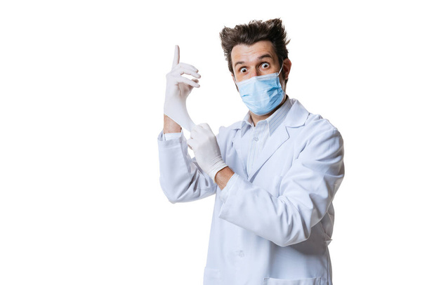 Portrait of young man, doctor wearing protective face mask and gloves isolated on white background. Concept of healthcare and medicine, war, help, treatment - Foto, afbeelding