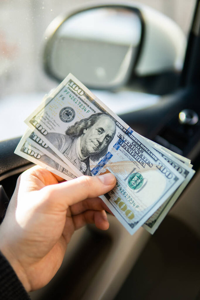 Billetes de un dólar en la mano masculina en el fondo del volante en el coche. Concepto de ganancias o sobornos, seguros o créditos, invertir o vender un automóvil
 - Foto, imagen