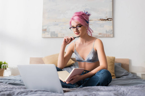 young woman with dyed hair holding pen and notebook while studying online at home - Zdjęcie, obraz