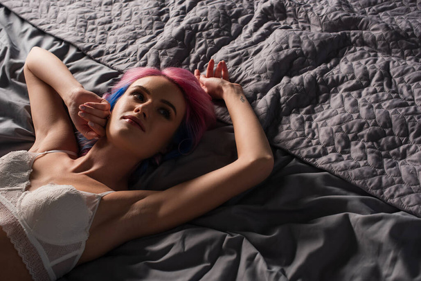 vista de ángulo alto de la mujer joven sexy con tatuaje en ropa interior de encaje acostado en la cama - Foto, Imagen