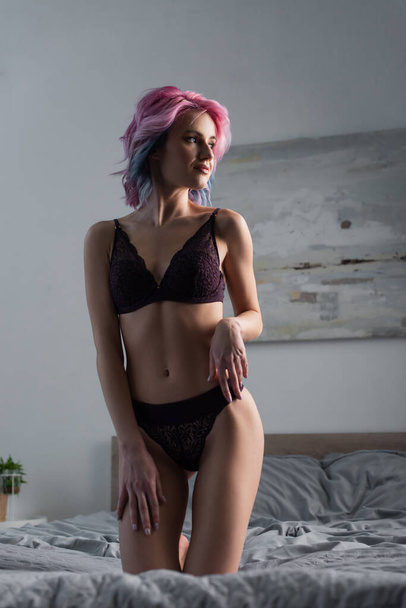 sexy woman with dyed hair in dark lingerie posing on bed at home - Fotografie, Obrázek