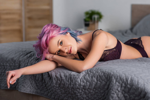 young woman in dark lingerie looking at camera and lying on bed - Valokuva, kuva