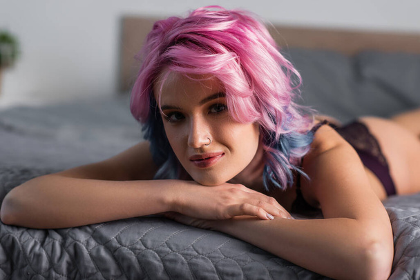 portrét mladé ženy s růžovými vlasy dívající se do kamery a ležící na posteli - Fotografie, Obrázek
