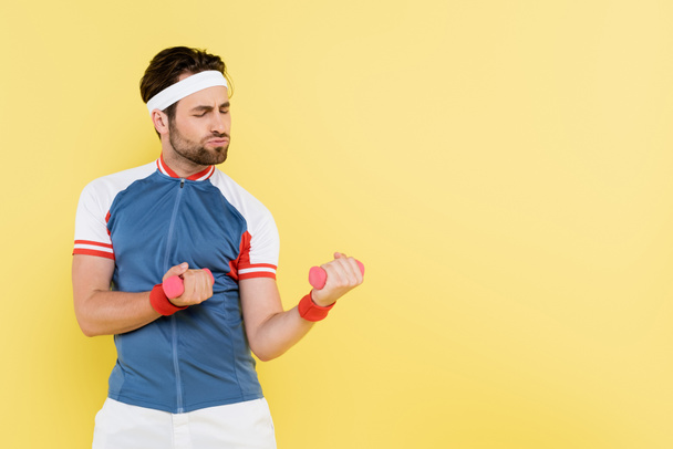 Sportsman in sports jacket training with dumbbells isolated on yellow  - Valokuva, kuva