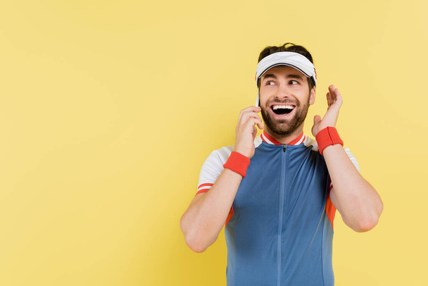 Deportista alegre hablando en smartphone aislado en amarillo  - Foto, Imagen