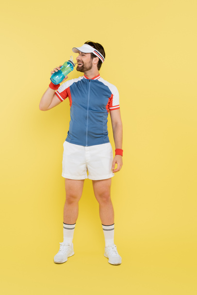 Full length of smiling sportsman holding sports bottle on yellow background  - 写真・画像