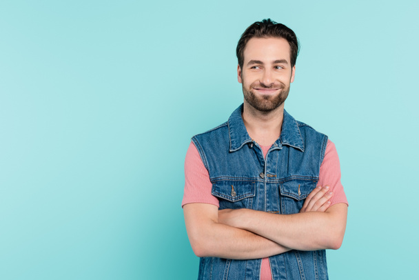 Smiling man in denim vest crossing arms isolated on blue  - Foto, immagini