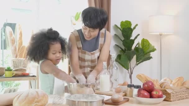 Familia afroamericana con madre que usa harina de trilla de delantal para cocinar y bailar con su hija juntos en la cocina en casa, padres e hijos pequeños que preparan alimentos con diversión y juguetón. - Metraje, vídeo