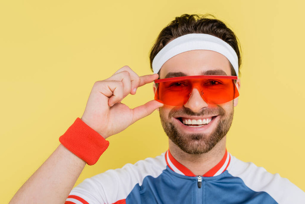 Happy sportsman holding sunglasses and looking at camera isolated on yellow  - Foto, Bild