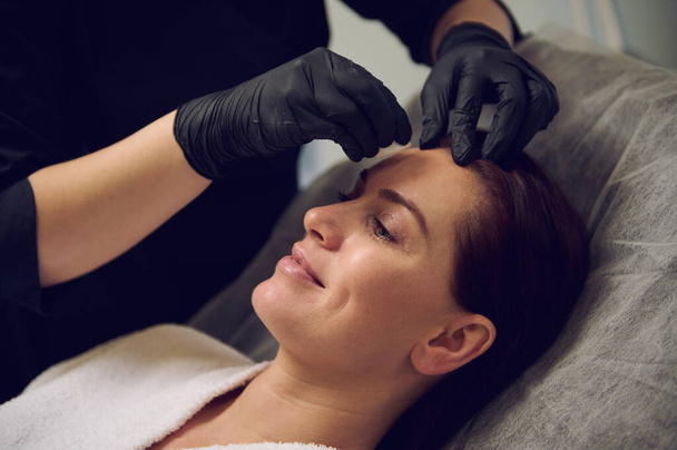 Close-up of a happy middle aged beautiful woman taking care of her face skin in modern wellness spa salon. Anti-aging anti wrinkles and rejuvenating beauty treatment. Health care and medicine concept - Photo, Image