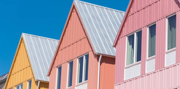 Açık mavi gökyüzü arka planına sahip, yeni geliştirilmiş renkli evlerin üstündeki metal çatının panorama görüntüsü. Wheeler Bölgesi, Oklahoma City, ABD yakınlarındaki iki katlı kasabaların ön cepheleri. - Fotoğraf, Görsel