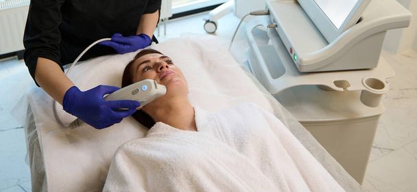 Houkutteleva valkoihoinen nainen saa anti-aging hoito hänen kasvonsa moderni laser laitteet wellness spa kosmetiikka klinikalla. Terveydenhuolto ja lääketiede, kauneudenhoito, ihotaudit - Valokuva, kuva
