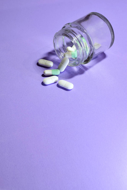 Tir vertical. Médicaments, dans des pilules sur fond mauve clair et dans un petit récipient en verre. Espace de copie. - Photo, image