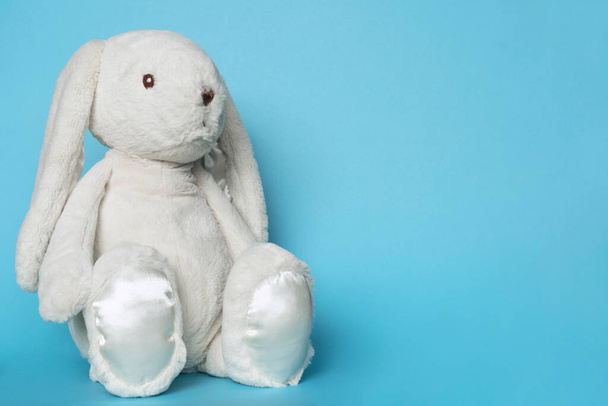 Gevulde konijn op blauwe achtergrond. Pasen concept. Beytiful wit speelgoed zacht konijn zitten op gekleurde achtergrond. Kopieer ruimte voor tekst - Foto, afbeelding