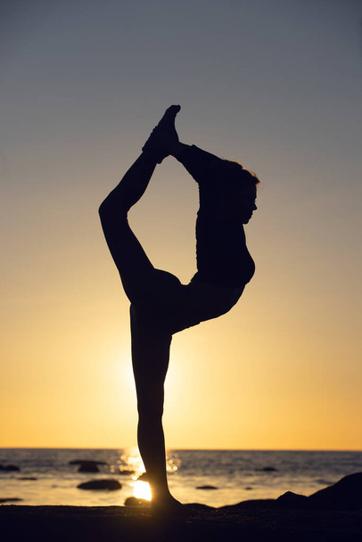 woman practicing stretching at sunset. seaside background, silhouette - Foto, Imagen