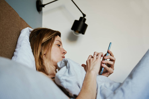 Жінка використовує смартфон в ліжку, соціальні медіа, ліниві вихідні
 - Фото, зображення