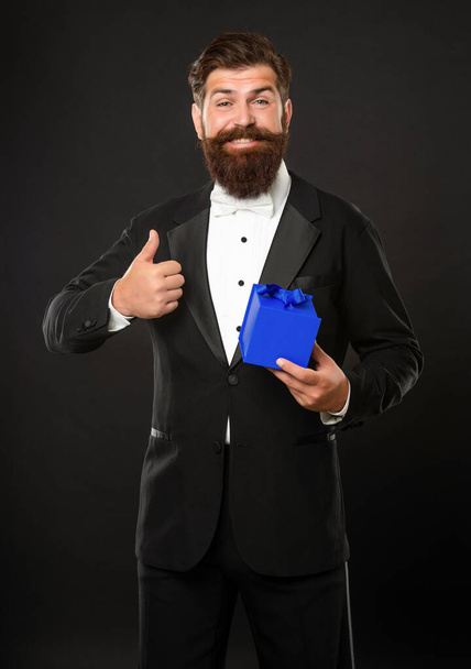 happy man in tuxedo bow tie formalwear on black background with box. birthday. thumb up - Фото, изображение