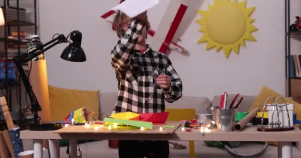 niño plegando un avión de papel y barcos, niño causasiático jugando con aviones de papel, futuro ingeniero diseñador, hobby - Metraje, vídeo