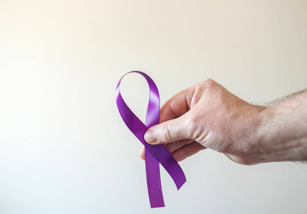 Uma mão masculina está segurando uma fita roxa. Epilepsia, cancro do pâncreas e símbolo de Alzheimer. - Foto, Imagem