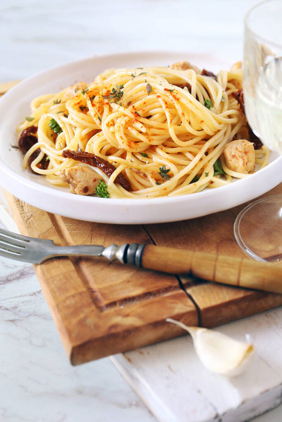 Ιταλική κουζίνα. Σπαγγέτι με λιαστή ντομάτα, σκόρδο ψητό κοτόπουλο και ποτήρι λευκό κρασί. Επιλεκτική εστίαση - Φωτογραφία, εικόνα