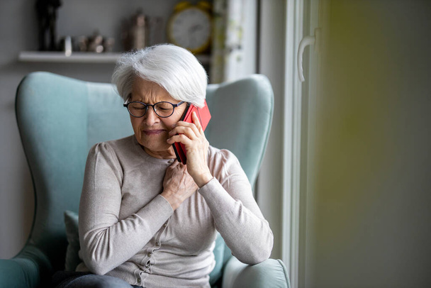 Ηλικιωμένη γυναίκα που αισθάνεται πόνο, ενώ συμβουλεύεται γιατρό στο έξυπνο τηλέφωνό της - Φωτογραφία, εικόνα