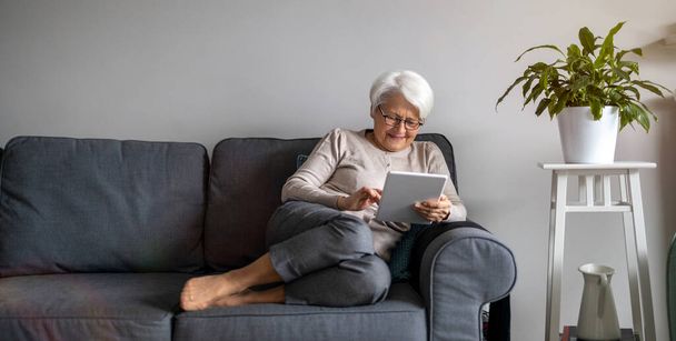 Vanhempi nainen, joka käyttää digitaalista tablettia kotona
 - Valokuva, kuva