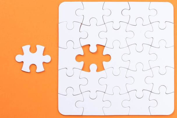 Puzzle pieces on orange surface. White jigsaw game grid texture. Matching, inserting last missing part. Business and teamwork problem solving background. Copy space for add text, close up. - Photo, Image