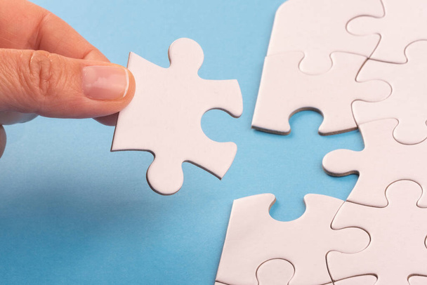 Hand holding Puzzle pieces on blue surface. White jigsaw game texture. Matching, inserting last missing part. Business and teamwork problem solving background. Copy space for add text, close up. - Photo, Image