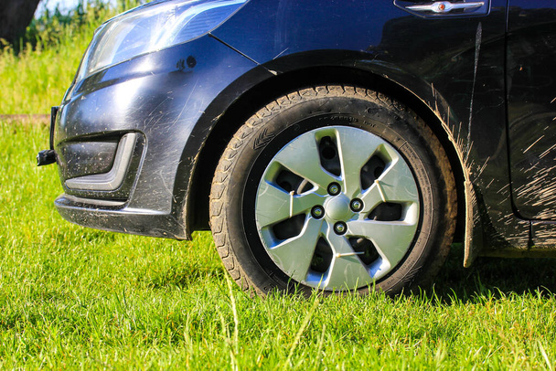 Kyiv, Ukraine.May 1, 2021. Black passenger car standing on a green grass on a lawn in summer day. Accent on a wheel, tire, rim, bumper. Dirty car requiring washing. Dirt splattered on the automobile. - Foto, Bild