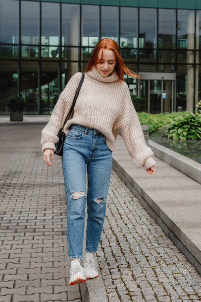 Portrait of successful happy woman on her way to work on street. Outdoor portrait of young beautiful natural redhead girl, very long hair, posing in street of city. Fashion girl with long red hair. - Fotó, kép