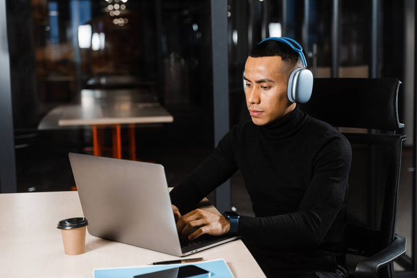 Asian man in headphones working online and listen to music in office. Asian handsome guy with laptop in coworking space - Fotoğraf, Görsel