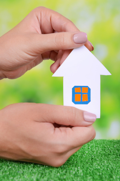 Woman hands holding paper house on grass on bright background - Photo, Image