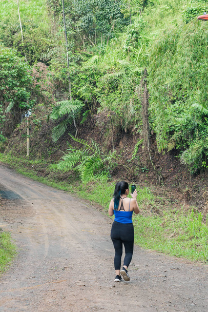 beautiful latin girl walking along a trail in the middle of a forest in colombia. capturing nature pictures with her cell phone. influencer walking through the jungle. hiking concept. - Fotoğraf, Görsel