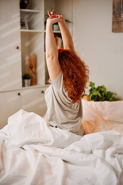 Egy vörös hajú lány reggel felébred és kinyújtja a karját.. - Fotó, kép