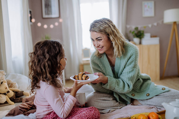 Szczęśliwa matka z córeczką jedzącą razem śniadanie w łóżku w domu. - Zdjęcie, obraz