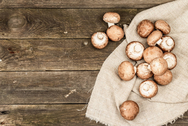 Fresh brown champignons in a wicker basket. Raw ingredients for cooking vegan food. Old wooden background, rustic style, top view - Foto, Bild