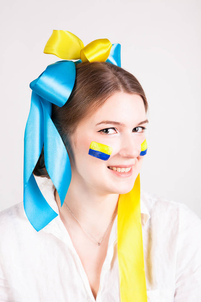 Onnellinen nuori nainen maalattu Ukrainan lippu poskillaan ja rusetteja eristetty valkoisella pohjalla. Ukrainan kansalliset värit. - Valokuva, kuva