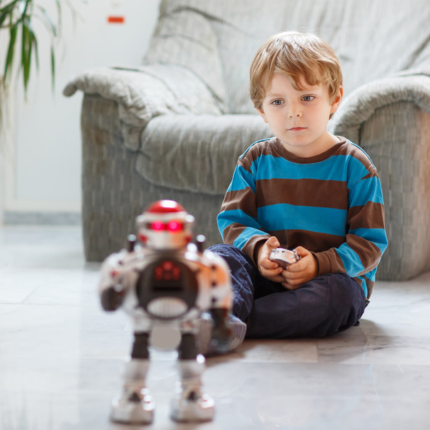 Little blond boy playing with robot toy at home, indoor. - Photo, Image
