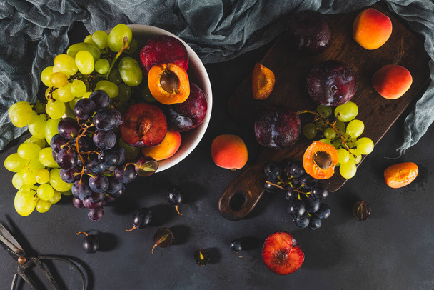 Vers gewassen fruit met waterdruppels. heldere high key look brengt frisheid. Verscheidenheid aan verse druiven, abrikozen en pluimen op donkere achtergrond. Fruitbronnen van vitaminen - Foto, afbeelding