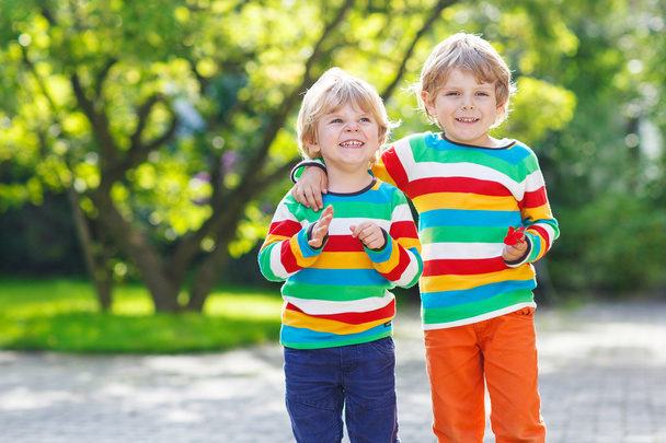 Two little kid boys in colorful clothing walking hand in hand - Photo, Image