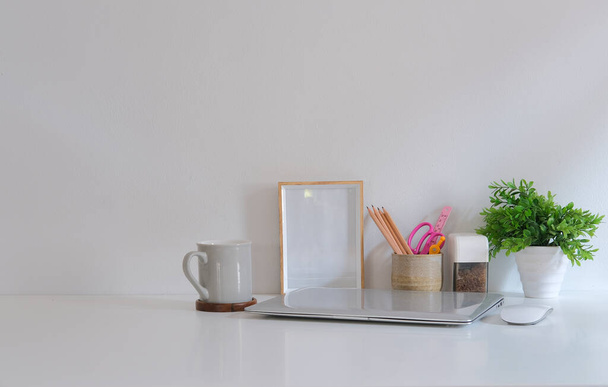 Bilderrahmen, Kaffeetasse, Topfpflanze und Laptop auf weißem Tisch. - Foto, Bild
