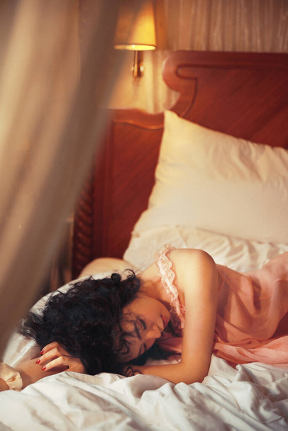 ベッドに横になってカメラを見ている若い美しい女性は - 写真・画像