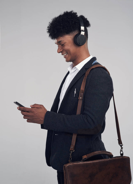 Η μουσική είναι η ζωή μου. Στιγμιότυπο ενός νεαρού επιχειρηματία που χρησιμοποιεί smartphone και ακουστικά σε γκρι φόντο. - Φωτογραφία, εικόνα
