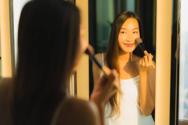 Muotokuva kaunis nuori aasialainen nainen muodostavat kosmeettinen jauhe ja huulipuna hänen kasvonsa kasvojen kylpyhuoneen sisustus
 - Valokuva, kuva